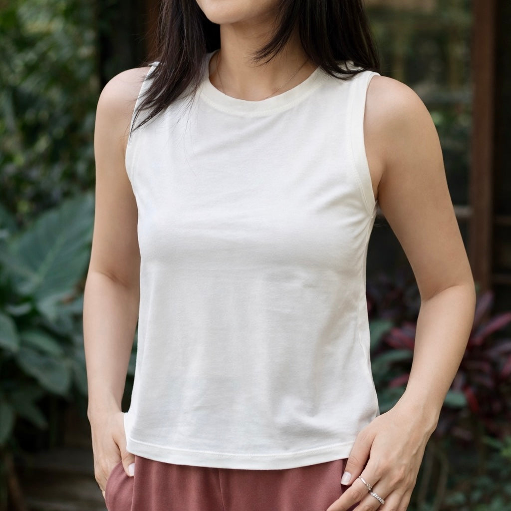 Person wearing a white sleeveless top with a blurred green background