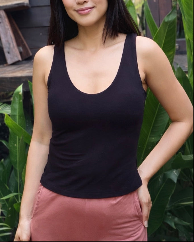 Woman wearing a black tank top and pink pants standing outdoors with greenery around.