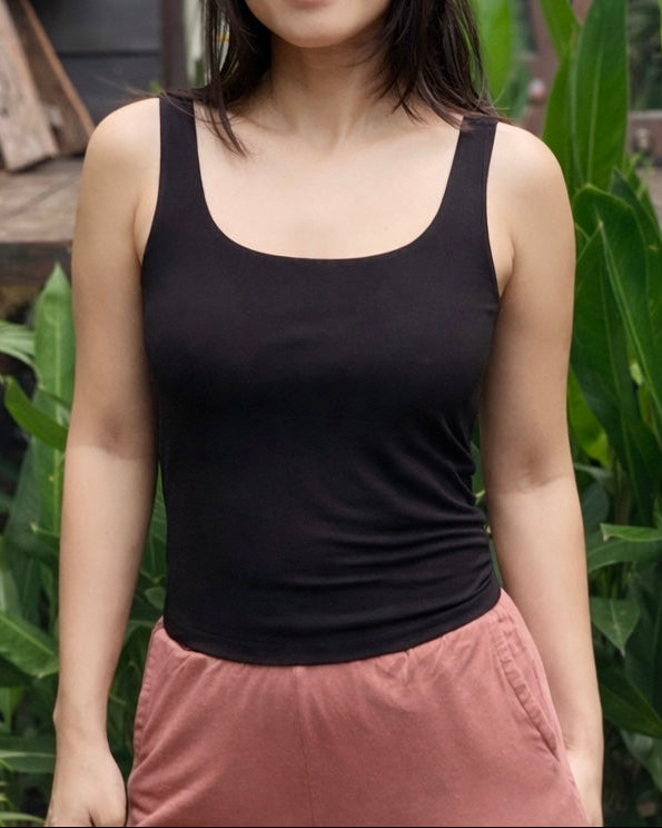 Woman wearing a black tank top and pink pants standing outdoors with greenery in the background
