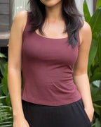 Woman wearing a maroon tank top with green foliage in the background