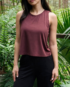 Woman wearing a chocolate plum top and black pants standing on a wooden deck with greenery in the background