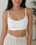A woman wearing a white scoop-neck spaghetti-strap bra and light beige drawstring sweatpants