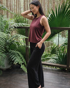 Woman in a maroon top and black pants standing on a wooden deck with greenery in the background
