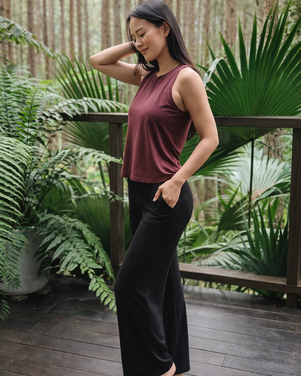 Woman in a maroon top and black pants standing on a wooden deck with greenery in the background