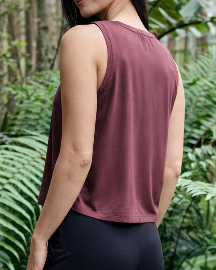Person wearing a mauve tank top with a blurred green forest background