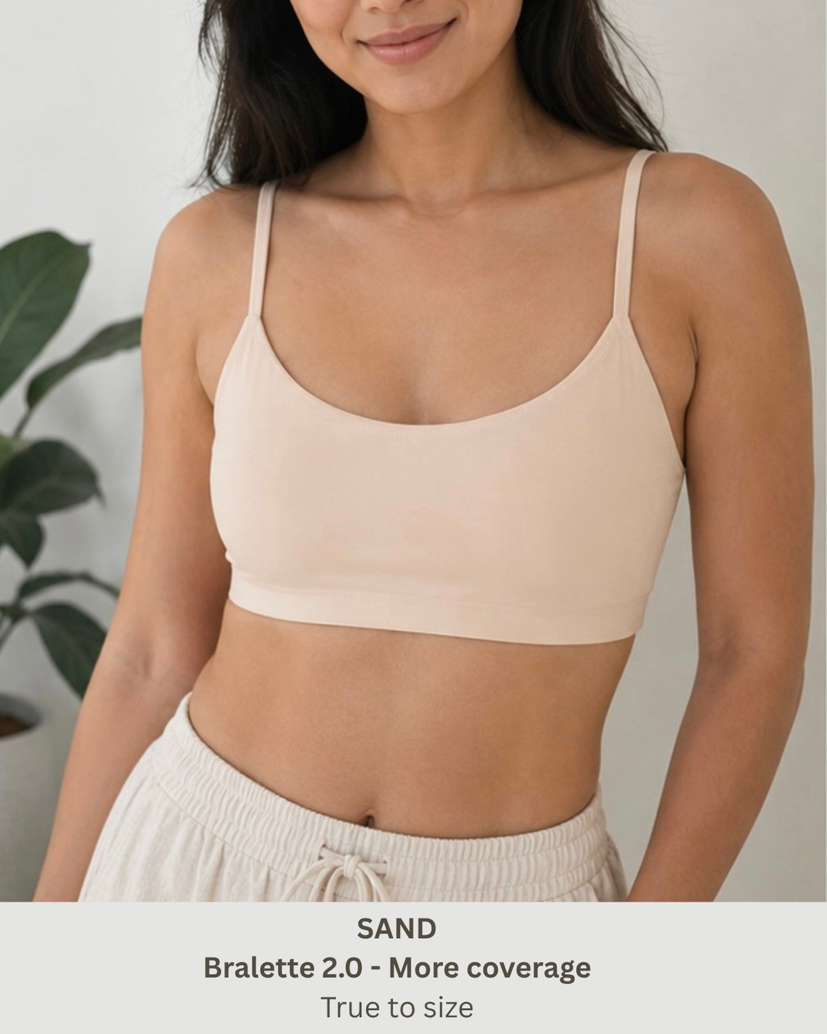 A woman wearing a sand-colored bralette crop top with thin straps and a wide underband, paired with light beige drawstring shorts. Text at the bottom reads 'SAND Bralette 2.0